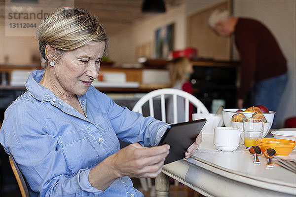 Frau benutzt Tablet-Computer  während der Ehemann mit der Enkelin im Hintergrund steht