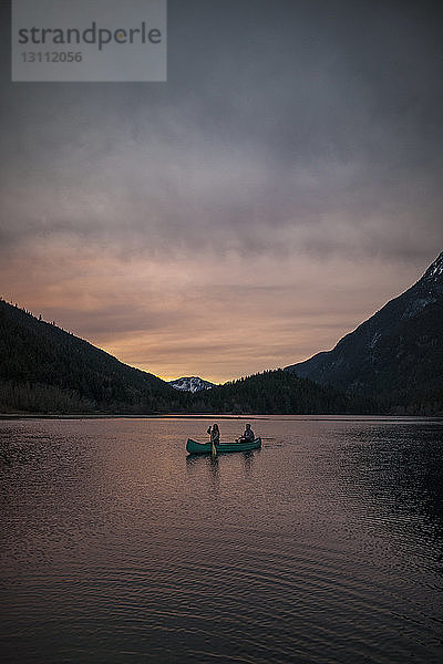 Mitteldistanzansicht eines Kanupaares auf dem See gegen Berge und Himmel während des Sonnenuntergangs im Silver Lake Provincial Park