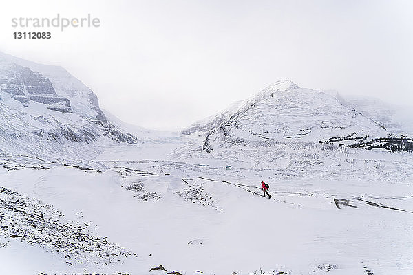 Mitteldistanzansicht eines Wanderers  der bei nebligem Wetter auf schneebedeckter Landschaft läuft