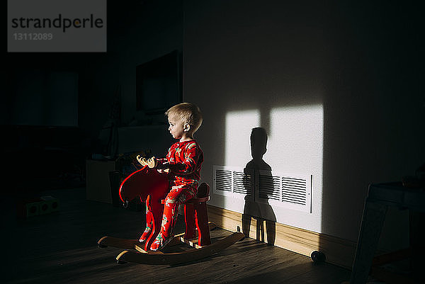 Kleiner Junge schaut weg  während er zu Hause auf einem Schaukelpferd sitzt