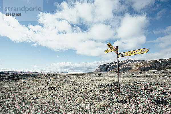 Straßenschild auf trockener Landschaft gegen bewölkten Himmel bei sonnigem Tag