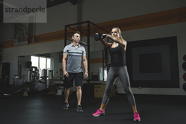 Trainer betrachtet Frau beim Heben einer Kesselglocke beim Training im Fitnessstudio