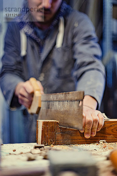 Mittelteil eines männlichen Tischlers beim Holzsägen in der Werkstatt