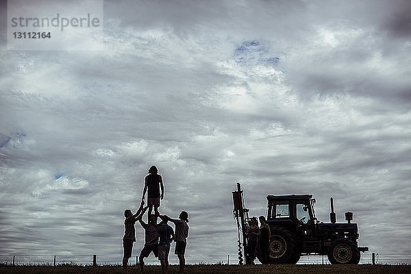 Freunde genießen es  auf dem Feld vor bewölktem Himmel am Traktor zu stehen