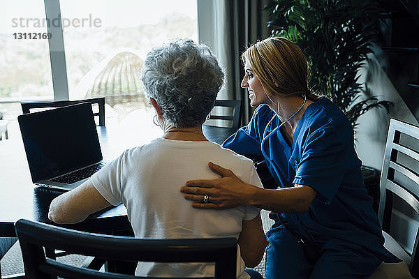 Hausangestellte diskutiert am Laptop mit älterer Frau am Esstisch