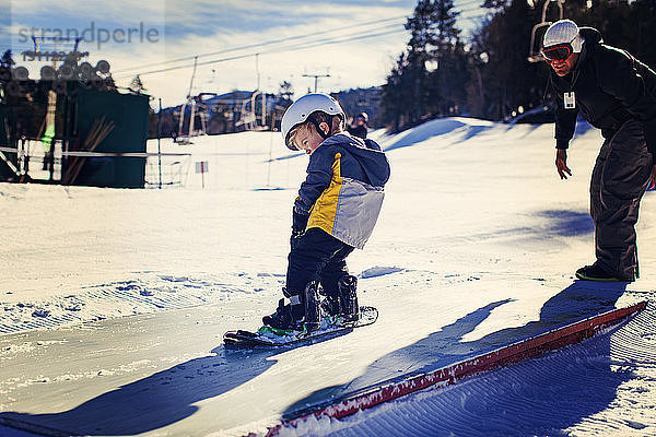 Vater assistiert Tochter beim Snowboarden an einem sonnigen Tag