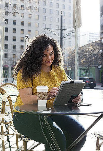 Frau benutzt Tablet-Computer  während sie auf einem Stuhl im Straßencafé in der Stadt sitzt