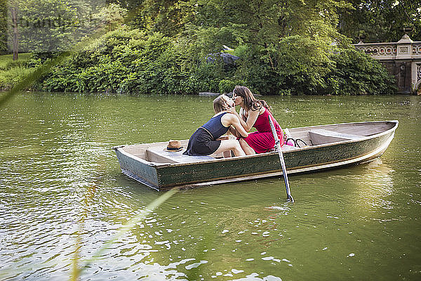 Lesbisches Paar küsst sich im Boot sitzend inmitten eines Sees