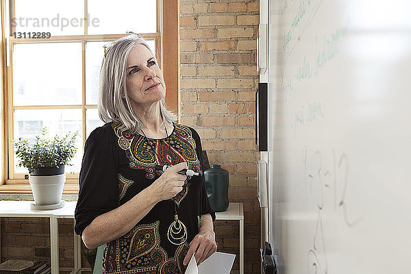 Reife Geschäftsfrau analysiert Strategie am Whiteboard im Kreativbüro