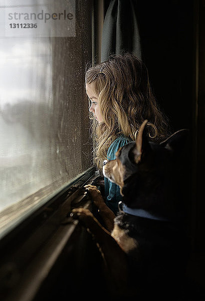 Seitenansicht von Mädchen und Hund beim Blick durch das Fenster in der Dunkelkammer