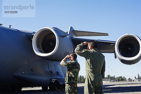 Armeesoldaten schirmen ab  während sie an einem Militärflugzeug auf der Landebahn stehen