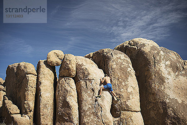 Rückansicht eines Mannes  der an Felsen klettert  die gegen den Himmel ragen