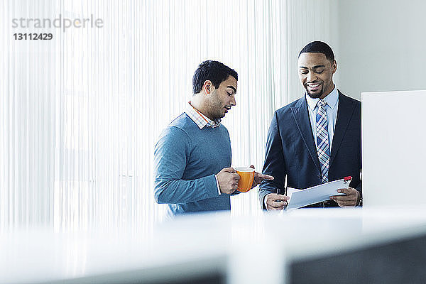 Geschäftsleute diskutieren über ein Dokument  während sie in einem hell erleuchteten Büro stehen