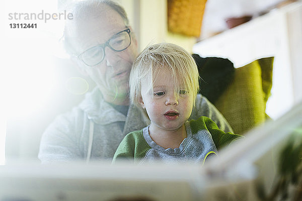 Niedriger Blickwinkel auf Großvater mit Enkelin beim Lesen eines Buches  während sie zu Hause sitzen