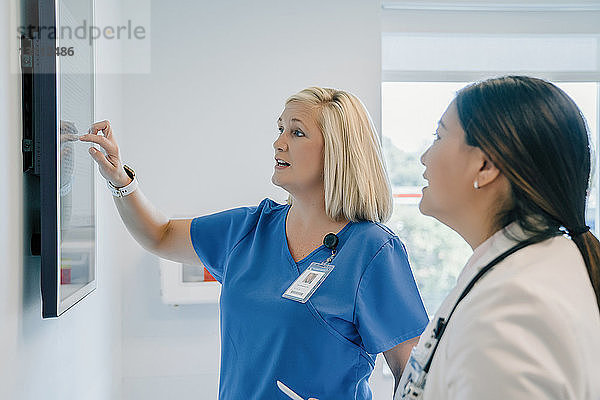 Ärztin zeigt auf Flachbildschirm  während sie mit einer Kollegin im Krankenhaus diskutiert