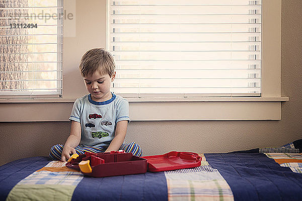 Junge spielt mit Spielzeug  während er zu Hause auf dem Bett sitzt