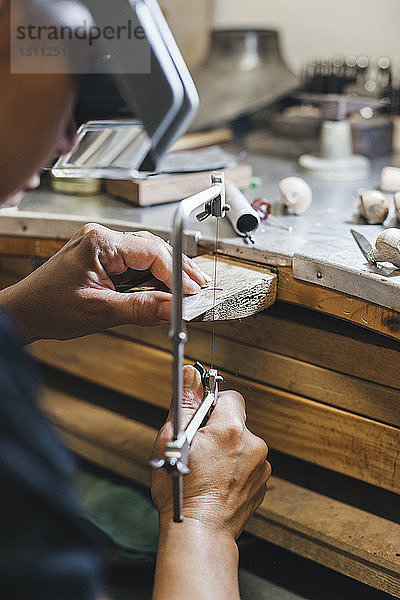 Beschnittenes Bild einer Handwerkerin  die mit einer Handsäge Schmuck auf einem Holztisch in einer Werkstatt herstellt