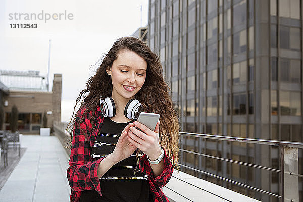 Junge Frau benutzt Smartphone beim Spaziergang im Terrassencafé