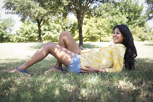 Glückliche schwangere Frau liegt auf Gras im Park