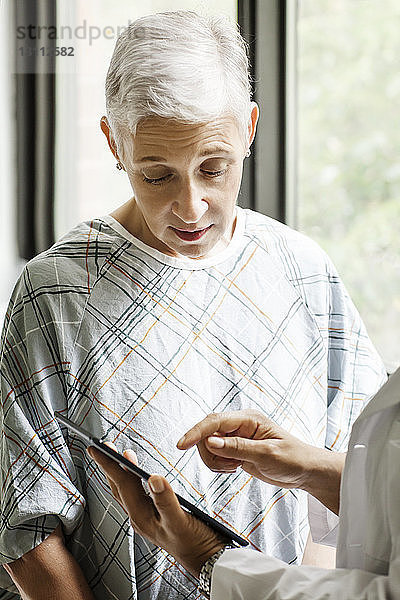 Ausgeschnittenes Bild eines Arztes  der dem Patienten einen medizinischen Bericht auf einem digitalen Tablett in der Klinik zeigt