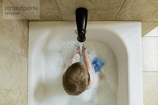 Draufsicht auf einen Jungen  der in der Badewanne mit Wasser spielt