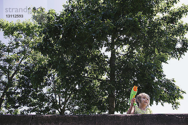 Niederwinkelansicht eines Mädchens  das eine Wasserpistole gegen Bäume hält