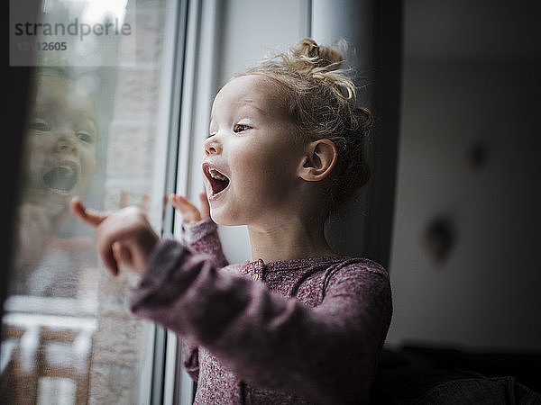 Zu Hause stehendes Mädchen mit offenem Mund  das durch ein Fenster schaut