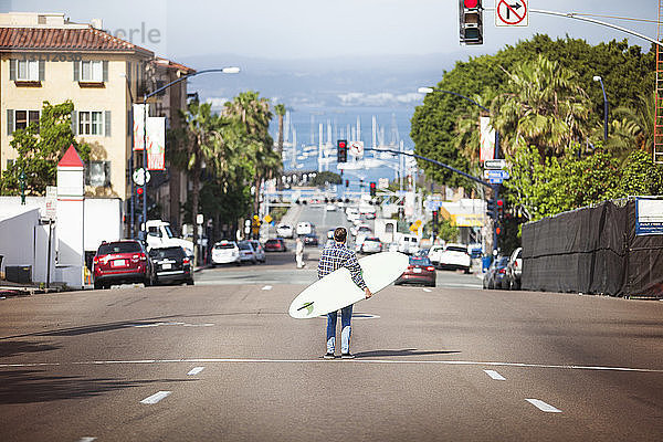 Rückansicht eines Mannes  der ein Surfbrett hält und auf der Straße steht