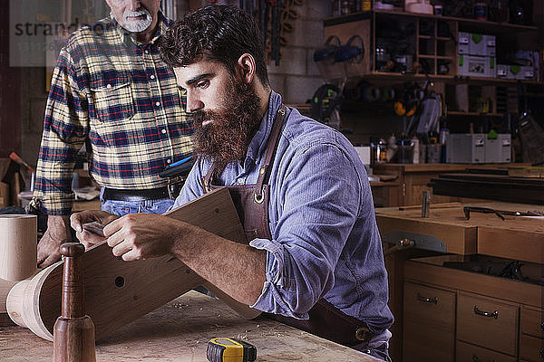 Älterer Mann steht neben männlichem Arbeiter  der Holz in der Werkstatt bearbeitet