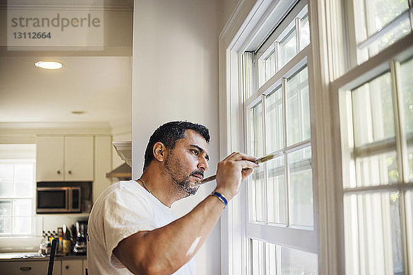Seitenansicht eines Mannes  der zu Hause Fensterrahmen malt