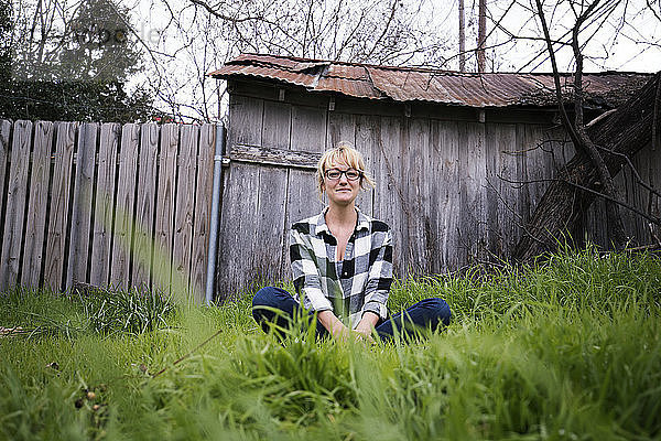 Porträt einer lächelnden Frau  die auf einem Grasfeld im Hinterhof sitzt