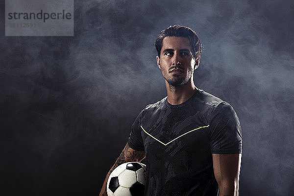 Nachdenklicher Fußballspieler steht vor schwarzem Hintergrund