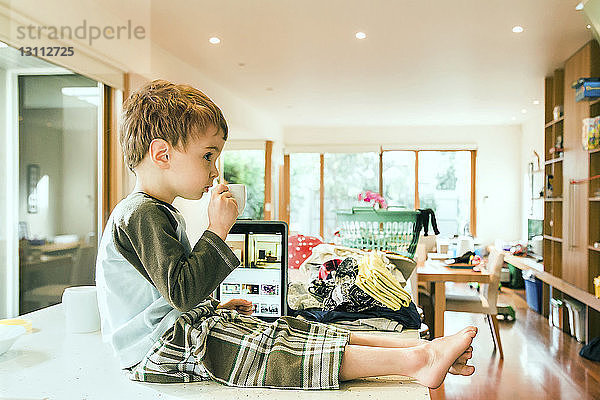 Seitenansicht eines süßen Jungen  der trinkt  während er zu Hause im Wohnzimmer am Tisch sitzt