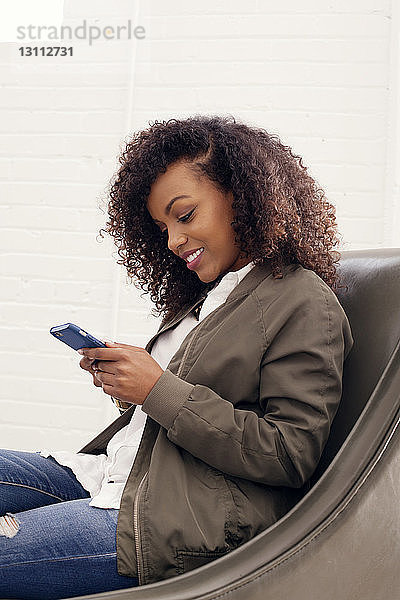 Selbstbewusste Geschäftsfrau telefoniert  während sie im Büro auf dem Sofa sitzt