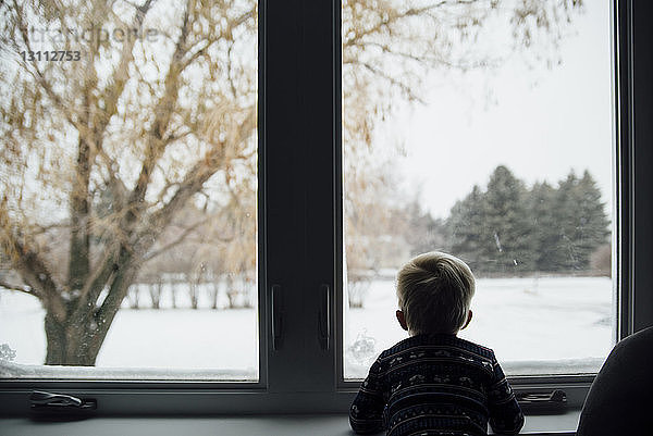 Rückansicht eines zu Hause stehenden kleinen Jungen  der durch ein Fenster schaut