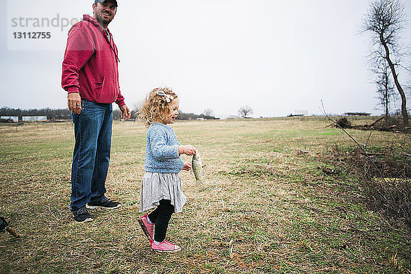 Fröhliche Tochter hält Fisch  während sie mit dem Vater auf einem Grasfeld fischt