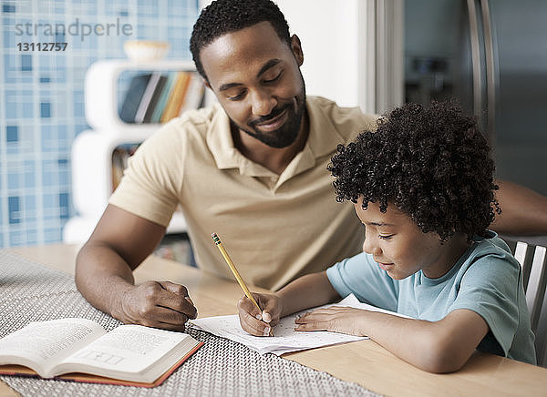 Vater hilft Sohn bei den Hausaufgaben bei Tisch zu Hause