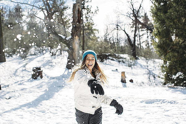 Frontansicht einer fröhlichen Frau  die mit Schnee auf dem Feld spielt