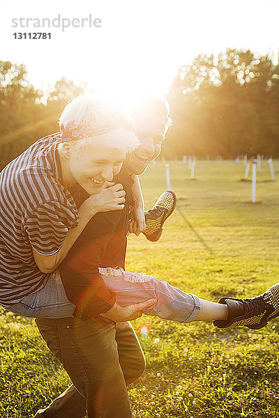Glücklicher Mann mit Huckepack-Freund bei Sonnenschein auf dem Spielfeld