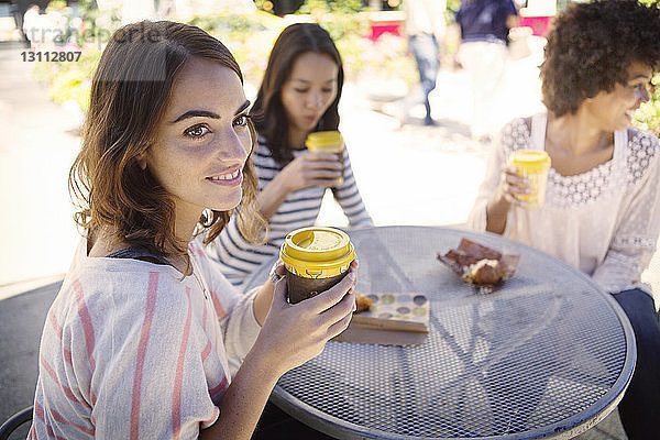 Freunde halten Kaffeetasse  während sie im Straßencafé sitzen