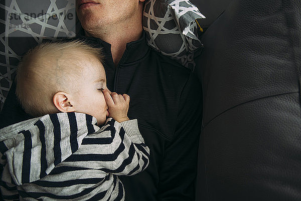 Draufsicht eines Jungen  der zu Hause auf dem Sofa mit seinem Vater schläft