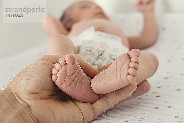 Ausgeschnittenes Bild einer Person  die die Füße des Babys auf dem Bett hält
