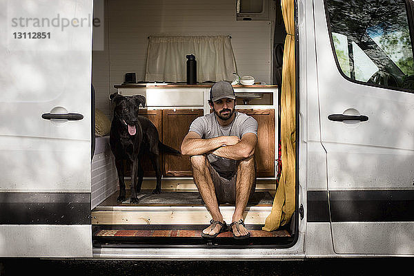Nachdenklicher Mann mit verschränkten Armen sitzt mit Hund im Wohnmobil
