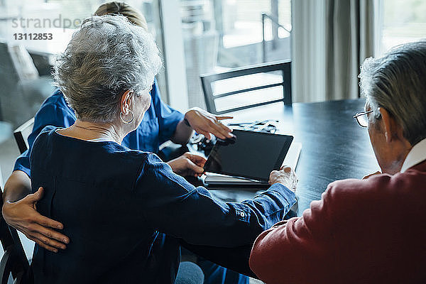 Hausangestellte diskutiert am Esstisch am Tablet-Computer mit einem älteren Paar