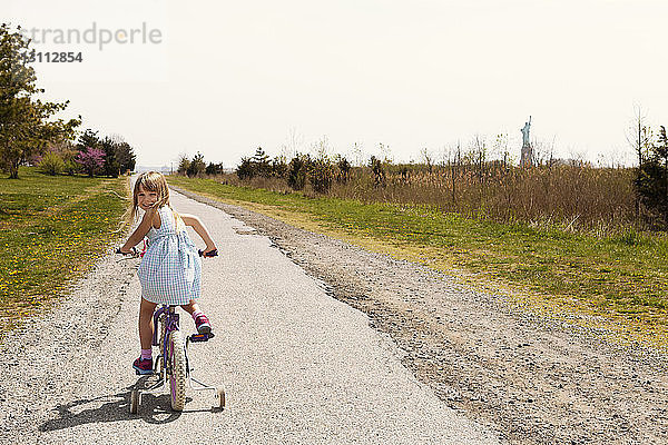 Rückansicht Portrait eines Mädchens auf dem Fahrrad auf der Straße inmitten des Feldes