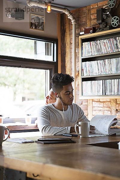 Mann hört Musik  während er im Café ein Buch liest