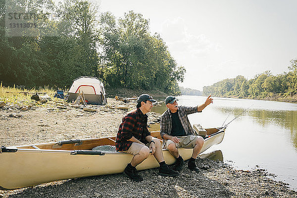 Männliche Freunde unterhalten sich  während sie auf einem Boot auf einem Campingplatz am See sitzen