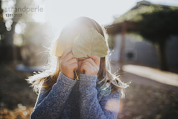 Mädchen versteckt Gesicht mit Blättern an sonnigem Tag