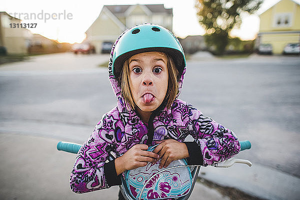 Porträt eines verspielten Mädchens mit herausgestreckter Zunge beim Rollerfahren auf dem Fussweg
