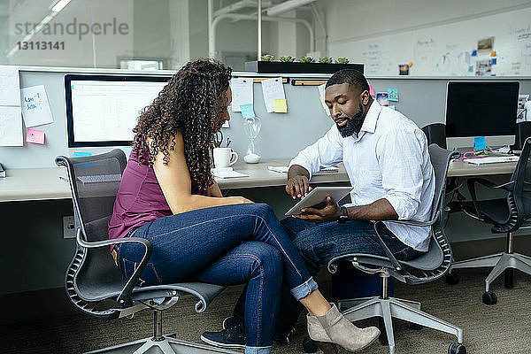 Geschäftsleute diskutieren über einen Tablet-Computer  während sie im Büro am Schreibtisch sitzen